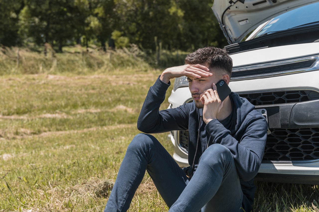 Man sitting down next to car calling for a Towing Service
